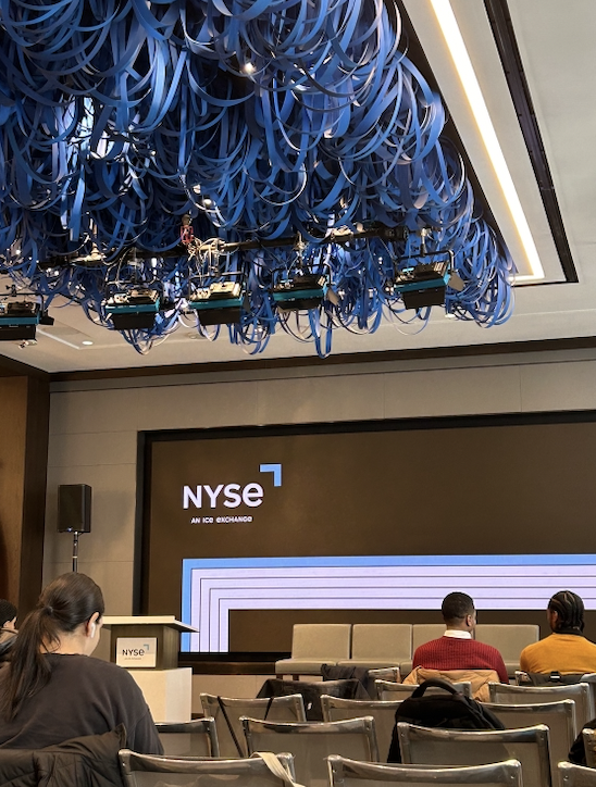 Some people sitting in a seminar room facing a large projector. An NYSE presentation is on-screen.
